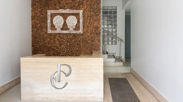 Recepção com bancada de travertino e o monograma EP em metal prateado, diante de um painel de madeira