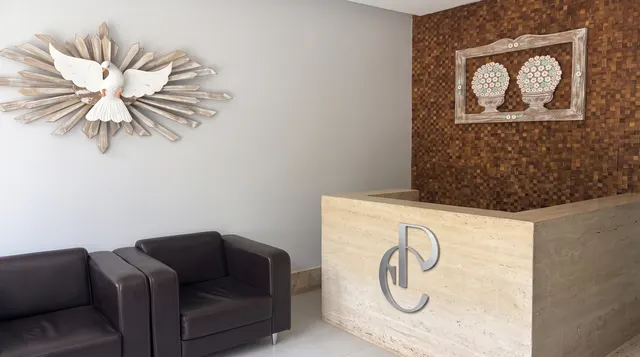 Recepção com poltronas de couro, escultura de pomba na parede e a bancada com o monograma EP