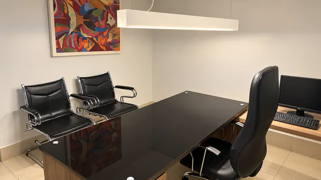 Sala individual com mesa de vidro preto, cadeiras de visitante e quadro colorido na parede